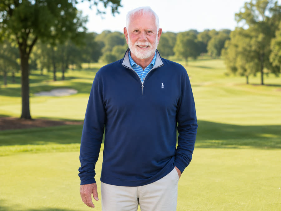 Monty mid-round on the golf course, smiling in a navy quarter-zip on a sunny day